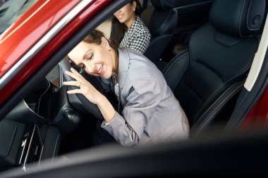 Neşeli bayan arabada oturuyor ve yüzünü direksiyona yaslıyor.