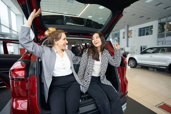 Gülümseyen Takım Elbiseli Kadınları Kırmızı Arabanın Bagajında Oturup Birbirlerine Bakıyorlar — Stok fotoğraf