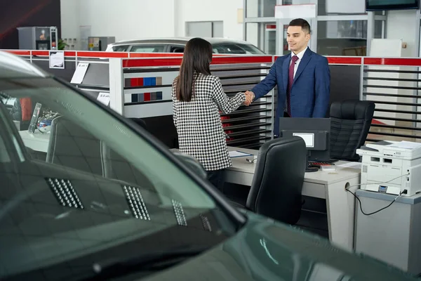 Smiling Salesman Cardealership Looks Woman Shaking Hands Standing Table — Stock Photo, Image