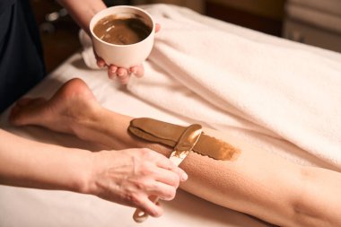 Güzellik uzmanının kadın müşteri baldırına spatula sürerken çekilmiş fotoğrafı.