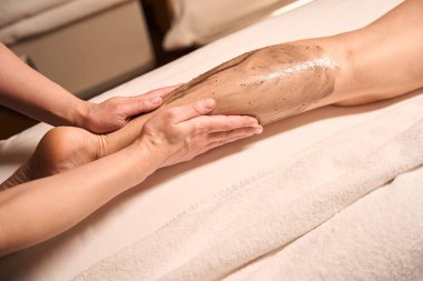 Kadın bacağına kahverengi yosun ezmesi sürten masöz ellerinin kesilmiş fotoğrafı.