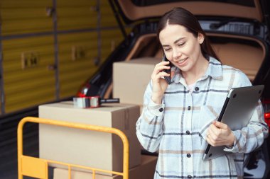 Telefonun yanındaki depoda elinde kutularla bekleyen neşeli bir kadın.