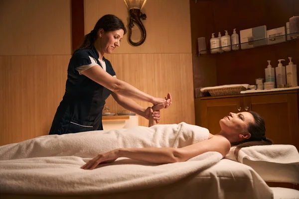Geconcentreerde Volwassen Masseuse Uniform Stretching Client Polsspieren Tijdens Massage Sessie — Stockfoto