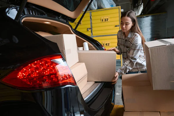 集中的成年女性站在仓库时 将货物装在箱子里装入汽车后备箱 — 图库照片