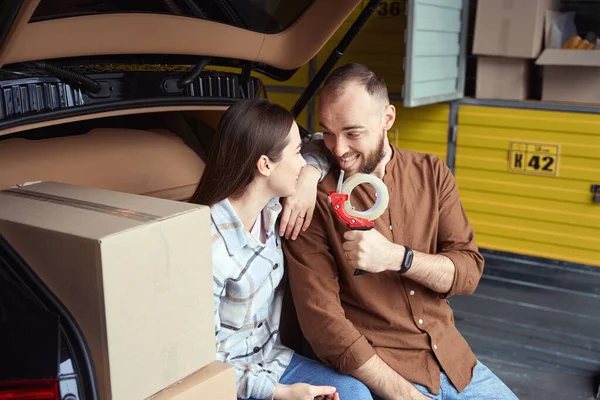 Grown Happy Man Showing Something Woman Sitting Trunk Car Warehouse — Stock Photo, Image