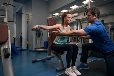 Gülümseyen kadın, kişisel antrenörün rehberliğinde halterde yükselen halterler sergiliyor.