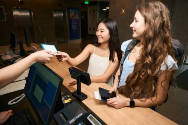 Gülümseyen kadınların resepsiyondaki odanın anahtarlarını teslim edişinin yan görüntüsü. Otelden çıkış.