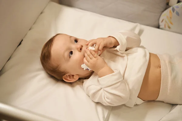 穏やかな小さな赤ちゃん置くプラスチック製のおもちゃ口の中に横にバックでクリブ — ストック写真