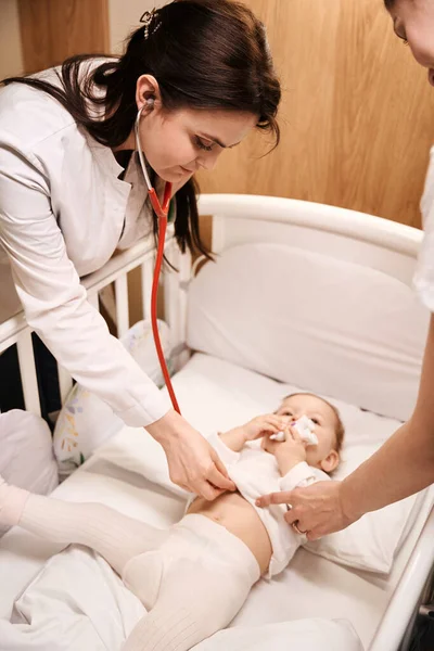 集中的女儿科医生在家长在场的情况下 用听诊器倾听新生儿的心跳 — 图库照片