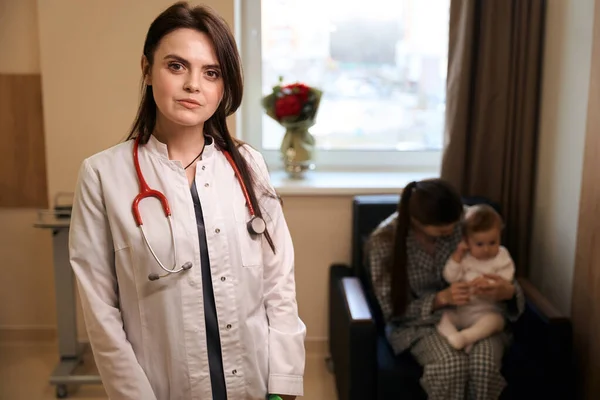 Arka Planda Annesi Küçük Çocuğu Olan Ciddi Bir Çocuk Doktoru — Stok fotoğraf