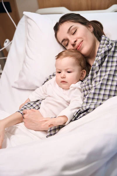 Uśmiechnięta Kobieta Leżąca Razem Swoim Smutnym Dzieckiem Szpitalnym Łóżku — Zdjęcie stockowe