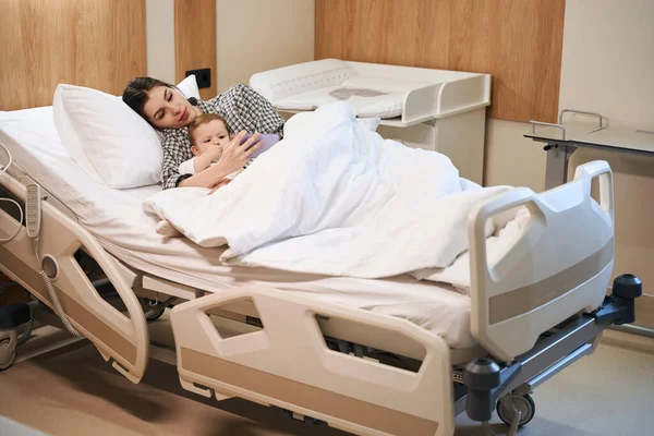 Женщина Помощью Смартфона Лежит Своим Больным Младенцем Больничной Койке — стоковое фото
