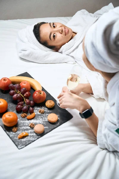 バスローブや果物のホテルのベッドの上で作物の写真の女性 女の子の友人一緒にベッドの上で果物を食べる — ストック写真