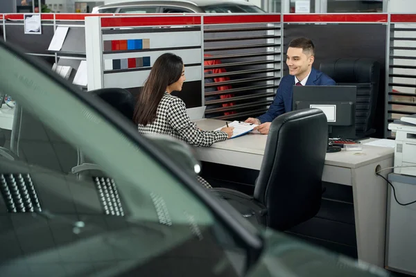 Young asian woman and car dealership manager communicate in office area, woman signs car purchase paperwork