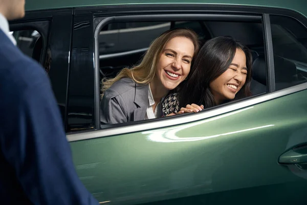 Joyful female lgbt couple on a car review before buying, next to a car dealership consultant