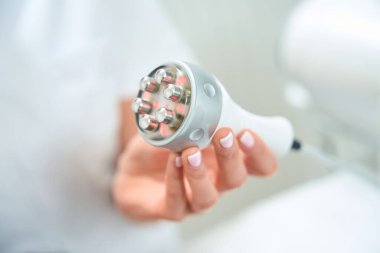 Güzellik uzmanı elinde bir radyo dalgası kaldırma aleti tutuyor. Kadının manikürü çok düzgün.