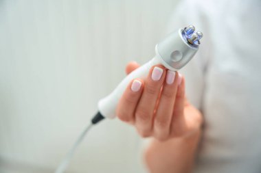 Kozmetik uzmanı, cerrahi olmayan kaldırma için RF cihazının başlığını elinde tutuyor. Kadının temiz bir manikürü var.