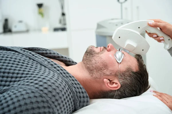 stock image Middle-aged man on a photorejuvenation procedure, a cosmetologist works with the frontal area