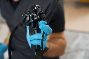 Endoskopistin, kameranın önünde eldivenli bir endoskopi tutarken çekilmiş fotoğrafı.