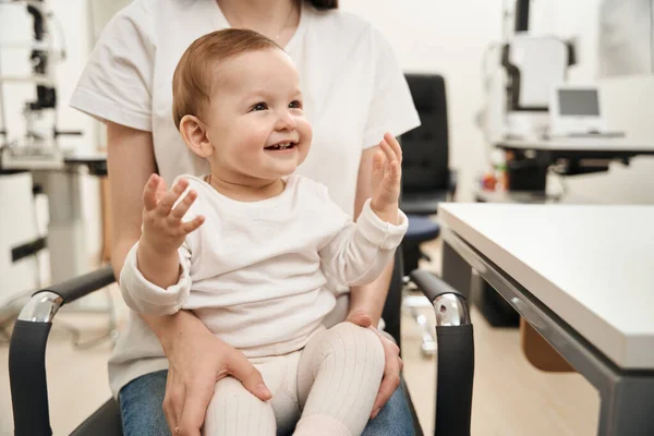 Joyous Baby Zittend Stoel Vrouwelijke Ouder Schoot Tijdens Het Gezichtsonderzoek — Stockfoto