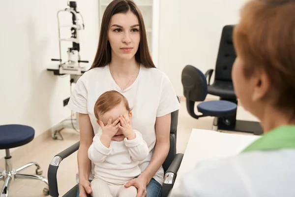Serious Woman Seated Child Chair Listening Pediatric Eye Doctor — Stock Photo, Image