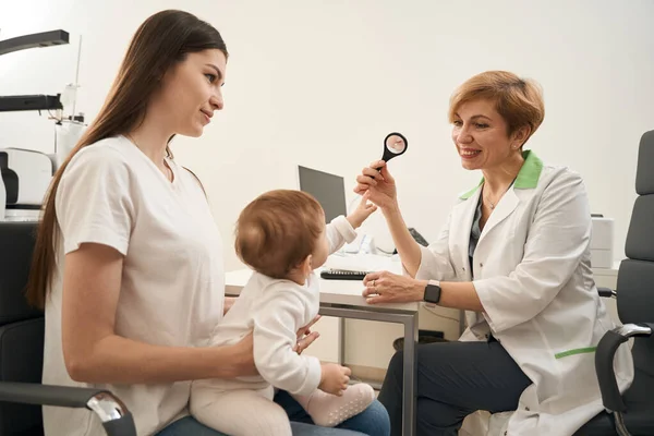 Vänlig Ögonläkare Som Håller Förstoringsglas Framför Barnet Sittande Stolen Mammas — Stockfoto