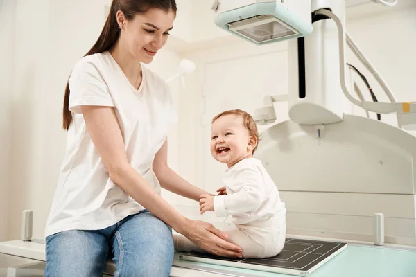 Memnun Genç Bayan Ebeveyn Bebeğini Özel Klinikteki Radyografik Masaya Yerleştiriyor — Stok fotoğraf