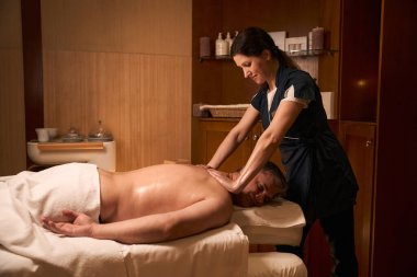 Profesyonel masaj terapisti, üst trapezius kasını müşterinin sırtına bastırıyor.