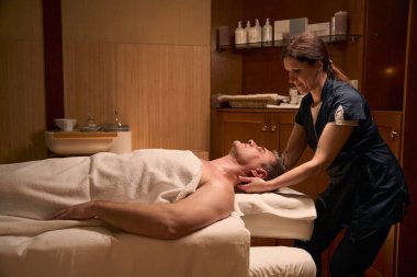 Deneyimli kadın osteopat osteopati seansı sırasında yetişkin bir erkek hastanın boynunu geriyor.