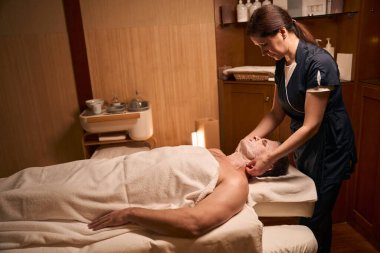 Ciddi kadın kozmetik uzmanının erkek yüzüne çarşaf maskesi takmasının yan görüntüsü