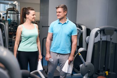 Havlu ve elinde bir şişe su olan memnun sporcu, fitness kulübündeki kız arkadaşıyla konuşuyor.