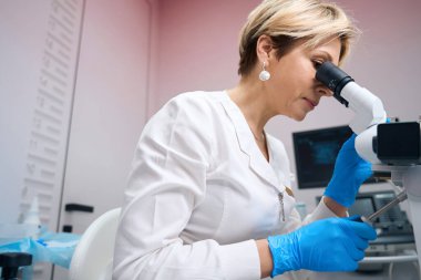 Odaklanmış kadın jinekolog mikroskopla analiz örneklerini dikkatlice inceliyor. Doktor jinekolog mikroskop kullanıyor.