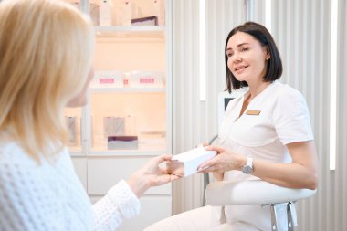 Kozmetik uzmanı müşterisine kozmetik ürünlerle dolu bir kutu veriyor. Profesyonel kozmetolog, bir kadın ziyaretçiye danışmanlık yapıyor.