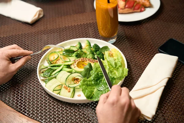 男子手拿刀和叉子在陶瓷盘上夹新鲜蔬菜沙拉的剪影 — 图库照片