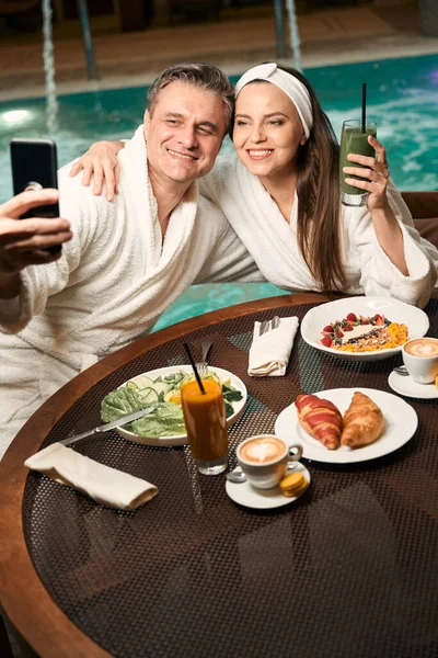 在游泳池拍照的时候 一个浪漫的女人在饭桌上拥抱她快乐的伴侣 — 图库照片