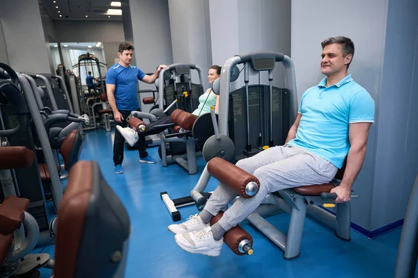 Glimlachende Vrouw Man Die Zittende Beenverlenging Uitvoeren Fitnessapparatuur Onder Leiding — Stockfoto