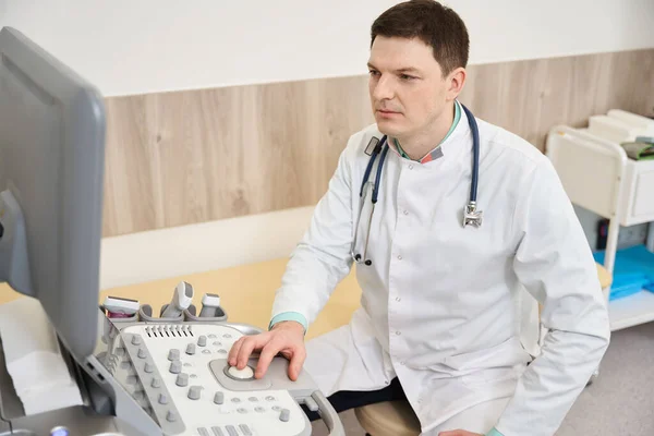 Beyaz Önlüklü Doktor Ekipmanın Yanında Oturuyor Hastanedeki Monitöre Bakıyor — Stok fotoğraf