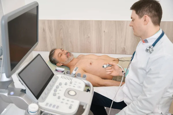 Beyaz Önlüklü Genç Doktor Ultrason Makinesinin Yanında Oturuyor Tarayıcıyı Tutuyor — Stok fotoğraf