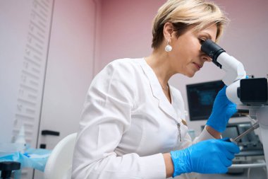 Odaklanmış kadın jinekolog mikroskopla analiz örneklerini dikkatlice inceliyor. Doktor jinekolog mikroskop kullanıyor.
