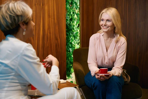 stock image Welcoming woman with cup of coffee in her hands smiling talking with gynecologist in spa salon