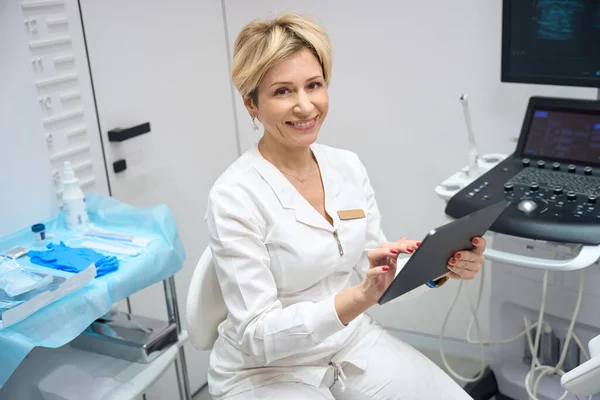 Χαμογελαστή Γυναίκα Γυναικολόγος Χρησιμοποιεί Ένα Gadget Στο Γραφείο Της Φόντο — Φωτογραφία Αρχείου