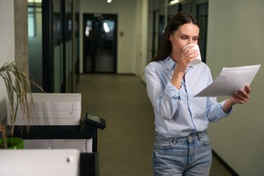 Koridorda fotokopi makinesinin yanında fotokopi çekerken odaklanmış kadın ofis çalışanı.