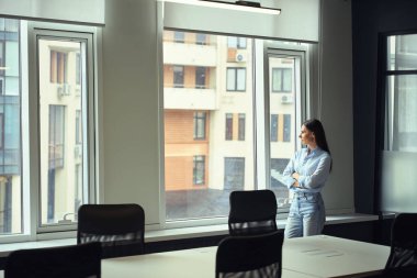 Düşünceli sakin kadın şirket çalışanı komşu yüksek binaya pencereden bakıyor.