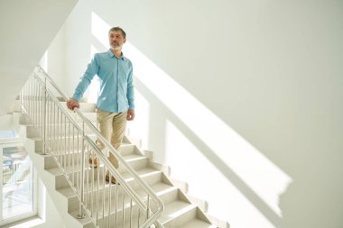 Tırabzanları tutan yakışıklı erkek beyaz bir iç mekânla kliniğin merdivenlerinden aşağı iniyor.