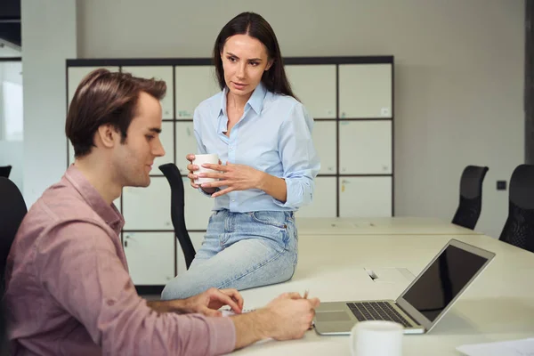 公司认真的员工 手里拿着茶杯坐在写字台上看着她忙碌的同事 — 图库照片