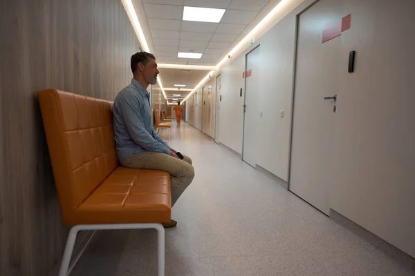 在医院长廊的一个医生办公室外的一张褐色的沙发上 成年男性在等待着 — 图库照片