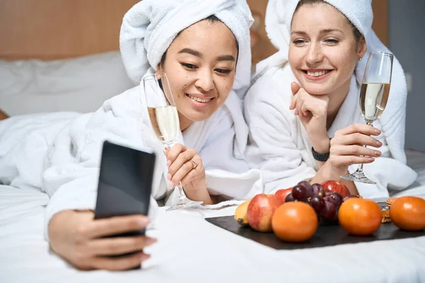 两个女人洗澡后在酒店房间里的自拍用眼镜和水果在手机上拍照 — 图库照片