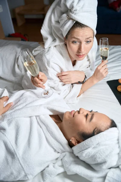 Beyaz Bornozlu Şampanyalı Iki Kadın Bir Otel Odasında Yatakta Uzanıp — Stok fotoğraf