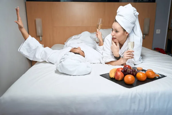 Retrato Namoradas Roupões Banho Com Óculos Frutas Falando Cama Hotel — Fotografia de Stock