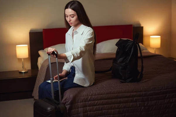 Young Woman Leaning Handle Suitcase Sitting Bed Hotel Room Looking — Stock Photo, Image